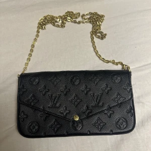 Svart axelväska  - Säljer en svart inte äkta axelväska från med klassiskt monogrammönster. Väskan har guldfärgad kedja och tryckknapp framtill.  