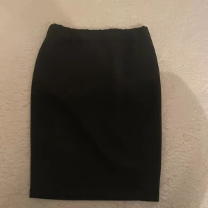 Svart tight pennkjol med resår - Enkel och stilren svart pennkjol med elastisk midja. Kjolen är tight och har en klassisk rak form som sitter snyggt. Perfekt för dig som gillar minimalistisk stil och vill ha en basic kjol i garderoben.