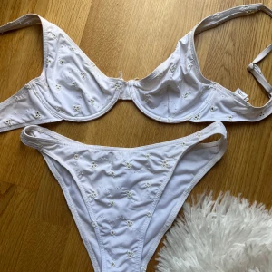 Vit blommig bikini från NA-KD - Superfin vit bikini från NA-KD med små broderade blommor över hela tyget. Överdelen har bygel och justerbara axelband, medan underdelen är högt skuren. 