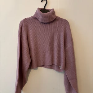 Ljuslila croppad polotröja - Superfin ljuslila polotröja med croppad passform och långa ärmar. Tröjan är ribbstickad och har en hög, mysig polokrage. Perfekt att styla med höga jeans eller kjol för en chill och trendig look.