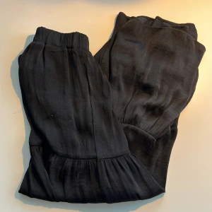 Svart maxikjol från Gina Tricot XXS - Svart maxikjol med volangdetalj från Gina Tricot i XXS. Stretchig resår och mycket bekväm under sommaren. Tyget är glansigt. 