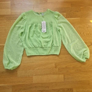 Grön blus med puffärmar från H&M - Superfin ljusgrön blus från H&M med transparenta puffärmar och små prickar i tyget. Smockad upptill och nertill för en snygg passform. Perfekt för dig som vill sticka ut med en färgglad och trendig topp.
