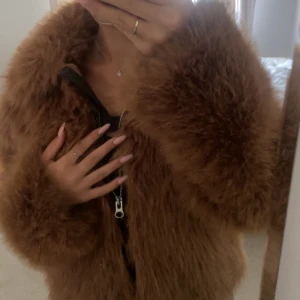 Brun fluffig pälsjacka med dragkedja - Supermysig brun pälsjacka med fluffig känsla och markerad krage. Jackan har en rejäl dragkedja framtill och är perfekt för dig som vill sticka ut. Passformen är loose och ärmarna är långa. Perfekt för kalla dagar när du vill vara både varm och snygg. Pris kan diskuteras