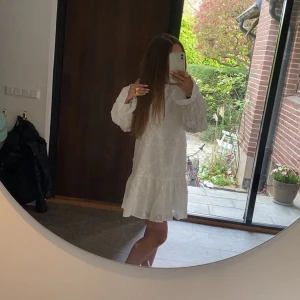 Vit broderad kortklänning med öppen rygg från NAKD - Superfin vit kortklänning med broderade blommor, volang nertill och långa puffärmar. Klänningen har öppen rygg med knytband. Endast använd 1 gång under min konfirmeration så säljer nu vidare den. Klänningen är från NAKD. Nypris är 699. Klänningen är i xxs, och klänningarna är stora i storlekarna.