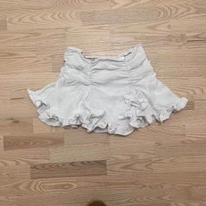 Vit volangkjol  - Supersöt vit kortkjol med volanger och rynkade detaljer i midjan. Kjolen har en flowy känsla och sitter snyggt i midjan. Perfekt för dig som gillar en feminin och trendig stil. Från weekday, använd ca 2 gånger