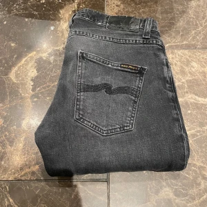 Nudie Grim Tim - Säljer dessa Nudie Jeans i modellen Grim Tim. Jeansen har en liten defekt i skrevet och inne i ficka men utöver det så är dom i fint skick. Färg: Mörkgrå. Hör av dig vid funderingar.