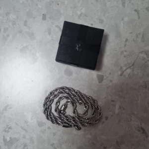 Silverfärgat tvinnat halsband - Snyggt halsband i silverfärg med tvinnad kedja som ger en cool och stilren look. Kedjan har ett smidigt lås och passar perfekt för dig som gillar minimalistiska accessoarer. Levereras i svart ask.