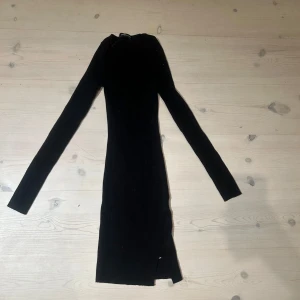 Svart långärmad klänning - Snygg svart ribbad klänning med lång ärm och tight passform. Modellen är kort och har en liten slits nertill för extra edge. Perfekt för dig som gillar minimalistisk stil med en twist.