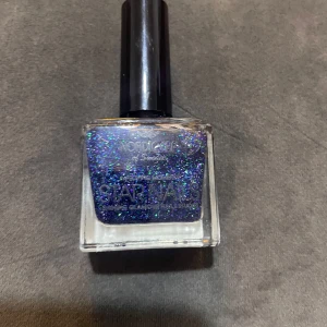 Glittrigt blått nagellack Star Nails - Snyggt nagellack från Nordic Cap of Sweden i serien Star Nails. Färgen är djupblå med massor av glitter i blått, lila och grönt. Kommer i en fyrkantig glasflaska med svart kork. Perfekt för dig som vill ha extra bling på naglarna.