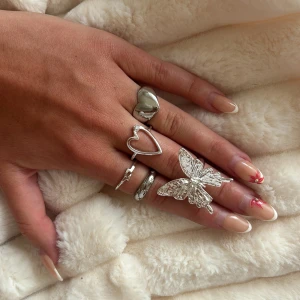 Set med silvriga ringar med hjärta & fjäril - Säljer ett set med fem silvriga ringar i olika former, bland annat en stor fjäril, ett öppet hjärta och en chunky hjärtformad ring. Perfekt för dig som gillar att mixa och matcha statementringar och skapa en unik look. Priser varierar lite beroende på vilka du köper!🩷