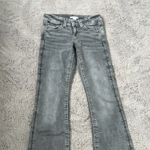 Grå bootcut jeans Gina Tricot 152 - Grå jeans från Gina Tricot i storlek 152. Modellen har bootcut-ben, klassiska fem fickor och snygga detaljer med knappar på bakfickorna. Jeansen har en tvättad look och är tillverkade i mjukt denimtyg.