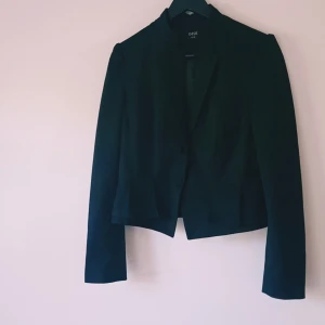 Svart kavaj från Oasis, storlek 38 - Stilren svart kavaj från Oasis i storlek 38. Klassisk modell med knappar framtill, lång ärm och lätt figursydd passform. Perfekt för dig som gillar en clean och snygg look. Snygg krage och diskreta fickdetaljer.  Helt & fint skick