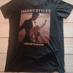 Harry Styles Live On Tour t-shirt svart S - Svart t-shirt från Harry Styles Live On Tour 2018 med stort tryck av Harry Styles på framsidan och turnédatum på baksidan. Rund hals och korta ärmar (OBS! halsringning har blivit klippt hemma, det är alltså inga sömmar runt halsringningen). Tillverkad i 100% bomull.