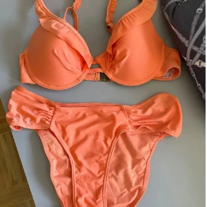 Orange bikini med volang från Lindex - Superfin orange bikini från Lindex med volangdetaljer på överdelen. Bikinin har vadderade kupor och axelband som går att justera. Underdelen har bredare sidor och en snygg, enkel design. Perfekt för stranden eller poolen i sommar! 75B/36 