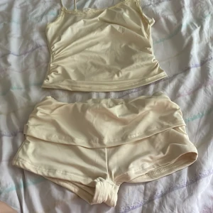Krämvit bikini med spetsdetalj - Snygg bikini i krämvit färg med linneinspirerad överdel och breda axelband. Överdelen har söt spetskant upptill och bikinitrosorna har hög midja och kortbensmodell. Materialet är glansigt och stretchigt, perfekt för strandhäng.