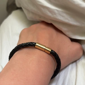 Svart flätat armband Skultuna - Stilrent svart armband från Skultuna med flätat band i läder och ett elegant magnetlås i guldmetall. Perfekt accessoar för dig som gillar en clean och modern look. Låset har Skultuna-loggan ingraverad för extra premiumkänsla. Använt 1 gång