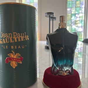 Jean Paul Gaultier Le Beau Parfym endast flaska (Tom) - Jean Paul Gaultier Le Beau Le Parfum i en unik flaska formad som en manlig överkropp i mörkblått glas med gulddetaljer. Kommer med original grön metallburk och röd sammetsbas. Det är inget kvar i den men Bra om man vill samla på parfym.