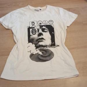 Håkan Hellström tröja(från 2020 typ) - Vit t-shirt från Neutral med coolt svart tryck framtill. Klassisk passform med rund hals och korta ärmar. Tillverkad i mjuk bomull som känns skön mot huden. Perfekt för dig som gillar grafiska motiv och enkel stil.