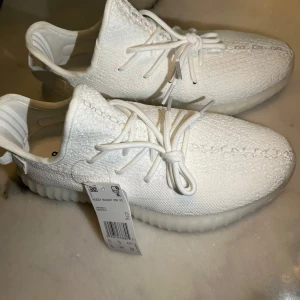 Adidas Yeezy Boost 350 V2 Triple White - Säljer ett par Adidas Yeezy Boost 350 V2 i helvitt. Skorna har stickad ovandel, tjock ribbad sula och klassisk snörning. Superclean look med diskreta detaljer och bekväm passform. Perfekta för dig som gillar stilrena sneakers med hype-känsla.