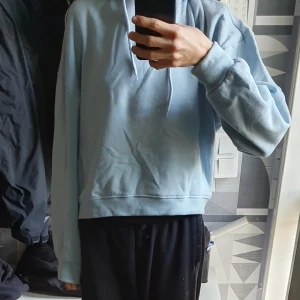 Ljusblå hoodie med huva - Säljer en ljusblå hoodie med huva och snörning. Tröjan har en relaxed fit med långa ärmar och breda muddar vid ärmslut och nederkant. Perfekt för chill dagar eller när du vill ha en enkel och stilren look.