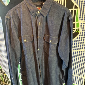 Levi's jeansskjorta relaxed fit L - Snygg mörkblå jeansskjorta från Levi's i relaxed fit. Skjortan har två bröstfickor med knappar, klassisk krage och kontrastsömmar. Perfekt för dig som gillar en avslappnad stil med denimkänsla.