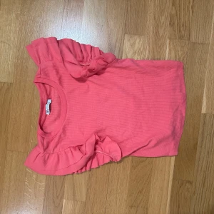 Rosa topp med volangärmar från H&M - Supersöt rosa topp från H&M med korta ärmar och volangdetaljer på axlarna. Perfekt för dig som vill ha något färgglatt och lekfullt i garderoben. Mjuk och skön bomullskvalitet som känns bekväm hela dagen.