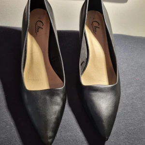 Svarta klackskor från Clou - Strl 41 - Snygga och eleganta klackskor från märket Clou i klassiskt svart. Storlek 41. Perfekta till fest, jobb, bröllop eller en utekväll! Använda väldigt lite och i fint skick. Stilrena med spetsig tå och bekväm passform.  🎯 Passar dig som vill ha både stil och komfort i ett par svarta klackar!  💸 Fynda dem second hand – både snyggt och hållbart!