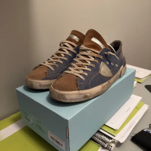 Philippe Model blå/bruna sneakers - Snygga sneakers från Philippe Model i blått och brunt med detaljer i mocka och skinn. Skorna har beige snörning, silverfärgad logga på sidan och platt sula. Perfekta för dig som gillar en avslappnad men trendig stil.