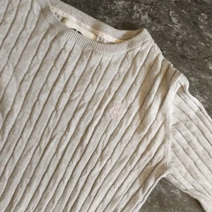 Ljusgrå kabelstickad tröja Hampton Republic - Kabelstickad ljusgrå tröja från Hampton Republic med rund hals och diskret broderad logga på bröstet. Tröjan har lång ärm och ribbade muddar vid hals, ärmslut och nederkant. Perfekt för dig som gillar klassisk och stilren look.