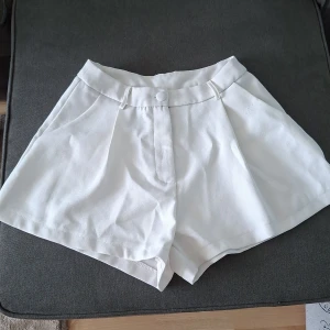 Vita högmidjade shorts från SHEIN - Snygga vita shorts från SHEIN med hög midja och vida ben. De har bälteshällor, knäppning med dold dragkedja och knapp framtill samt diskreta fickor i sidorna. Perfekta för en fräsch och clean sommarlook.