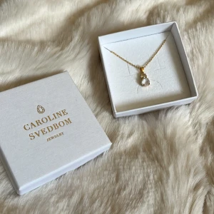 Guldigt halsband Caroline Svedbom - Superfint halsband från Caroline Svedbom med tunn guldpläterad kedja och hängsmycke med två gnistrande stenar. Klassisk och elegant design som lyfter vilken outfit som helst. Kommer i originalask. Nypris 429kr. 🤍