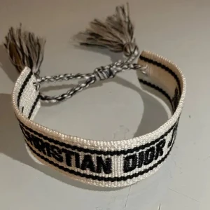  Dior armband  - Snyggt armband från Christian Dior i vitt tyg med svarta broderade detaljer och text. Nypris 3500 kr. Mitt pris 699