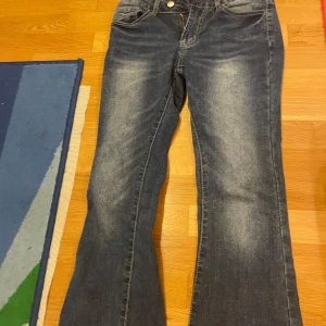 Blå bootcut jeans med slitningar - Snygga blå jeans med bootcut-modell och lätt slitna detaljer på låren. Klassisk femficksdesign och dragkedja fram. Jeansen har en normal passform och är perfekta för en avslappnad stil.