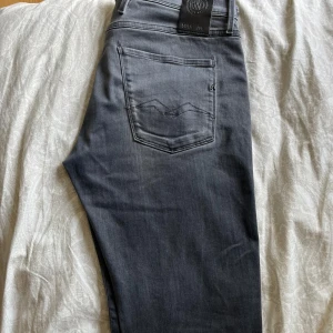 Grå jeans från Replay straight fit - Säljer ett par grå jeans från Replay med klassisk femficksdesign och diskret broderad bakficka. Jeansen har rak passform och är tillverkade i mjukt denimtyg som sitter skönt hela dagen. Perfekta för dig som gillar en clean och stilren look.