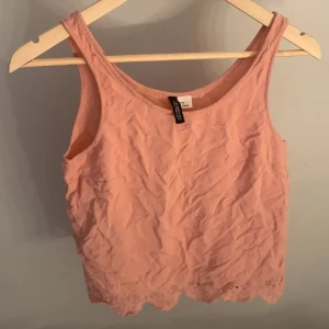 Rosa linnetopp med spetskant - Supersöt ljusrosa linnetopp från Divided med broderad spetskant nertill. Toppen är ärmlös och har en rak, croppad passform som passar perfekt till sommaren. Enkel och stilren design som är lätt att matcha med jeans eller kjol.