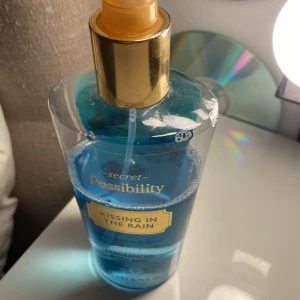 Passibility Kissing in the Rain Body Mist - Fräsch body mist med doft av blå fresia och dagg, i en genomskinlig plastflaska med guldigt spraymunstycke. Vätskan är klarblå och flaskan rymmer 200 ml. Perfekt för dig som gillar lätta, blommiga dofter.