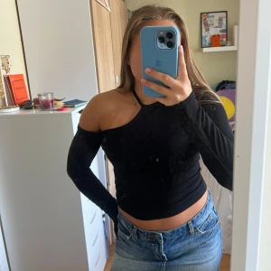 Svart oneshoulder croppad topp - Säljer en svart ribbad topp med oneshoulder-design och lång ärm. Toppen är croppad och sitter tight. 