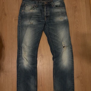 Nudie Jeans Big Bengt blå jeans W32 L32 - Säljer ett par blå Nudie Jeans Big Bengt i modellen Dirt Second Hand. Jeansen har slitna detaljer och hål på benen för en cool, använd look. Klassisk femficksmodell med raka ben och snygga kontrastsömmar. Tillverkade i 100% bomull.