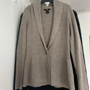 Beige stickad cardigan jacka H&M S - Snygg beige stickad cardigan jacka från H&M i storlek S. Jackan har en ribbad struktur, långärmad design och en knapp framtill. 