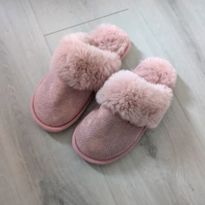 Fluffiga rosa tofflor med päls - Supermysiga tofflor i ljusrosa med fluffig fuskpäls över foten och mjuk sula. Perfekta att glida runt i hemma när du vill ha det extra cozy. Snyggt glittrigt tyg på ovansidan och riktigt skön känsla för fötterna. Enbart testade. Säljer då de är för små för mig.