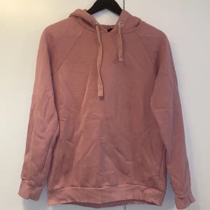 Rosa hoodie från Gina Tricot - Mysig hoodie i dammigt rosa från Gina Tricot. Tröjan har huva med snörning, långa ärmar och ribbade muddar. Perfekt för chill dagar och enkel att matcha med jeans eller leggings. Tillverkad i mjuk bomullsblandning för extra komfort.