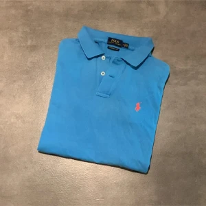 Blå pikétröja Polo Ralph Lauren - Snygg blå pikétröja från Polo Ralph Lauren i modellen The Skinny Polo. Klassisk krage, korta ärmar och knäppning framtill. Ikoniska röda loggan broderad på bröstet. Perfekt för en chill och stilren look. Tröjan ör i storlek L i barn och är blekt på några ställen som ni ser på bilderna. Bara att höra sv sig vid frågor eller funderingar! Pris kan diskuteras vi snabb affär😀
