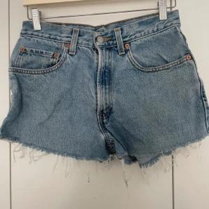 Levi's ljusblå jeansshorts med fransar - Ljusblå jeansshorts från Levi's, modell 550, med relaxed fit och rå fransig kant nertill. Klassisk femficksdesign, bälteshällor och knappgylf. Tillverkade i 100% bomull för en äkta denimkänsla. Perfekta för sommaren och en avslappnad stil.