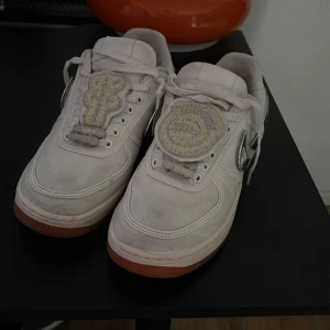 Nike Air Force 1 Travis Scott vita - Nike Air Force 1 Travis Scott🌵 i vitt tyg med gummisula i brunt. Skorna har utbytbara metallic-swooshes i silver och unika patches på plösen. Klassisk rund tå och snörning. Perfekta för dig som vill sticka ut med en ikonisk sneaker. Ingen original box tyvärr 📦