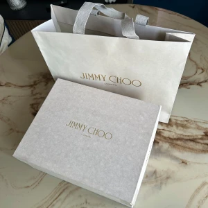Jimmy Choo klackskor - Supersnygga svarta klackar från Jimmy Choo i lackat skinn med spetsig tå och hög klack. Skorna har en glittrande rem med strass över foten som ger extra lyxig känsla. Perfekta för dig som vill sticka ut med elegans och stil.