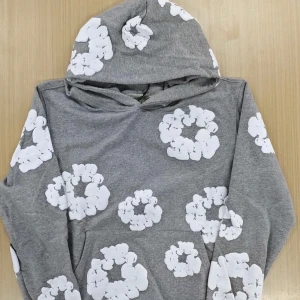 Grå hoodie från Denim tears - Grå hoodie från denim tears for Sports i storlek M med stora vita blommönster över hela tröjan. Mjuk bomullskänsla, huva och klassisk känguruficka framtill. Perfekt för dig som gillar en chill och unik stil.