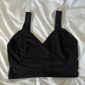 Svart croppad linnetopp - Snygg svart croppad linnetopp med breda axelband och v-ringad front. Enkel och stilren design som passar perfekt till höga jeans eller kjol. Gjord i mjuk bomull för en bekväm känsla hela dagen.