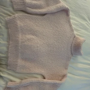 Ljusrosa stickad polotröja - Mysig ljusrosa stickad polotröja med lång ärm och breda ribbade muddar vid ärmslut, nederkant och krage. Perfekt för kyliga dagar och enkel att matcha med jeans eller kjol.