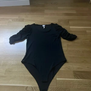 Svart bodysuit med puffärm från H&M - Säljer en svart bodysuit från H&M med rund halsringning och puffade långärmar. 