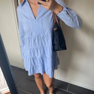 Ljusblå volangklänning  - Supersöt ljusblå klänning från med volanger och v-ringning. Klänningen har lång ärm och en avslappnad passform, perfekt för vår och sommar. Mjuk och lätt i bomullsmaterial. Bra skick!